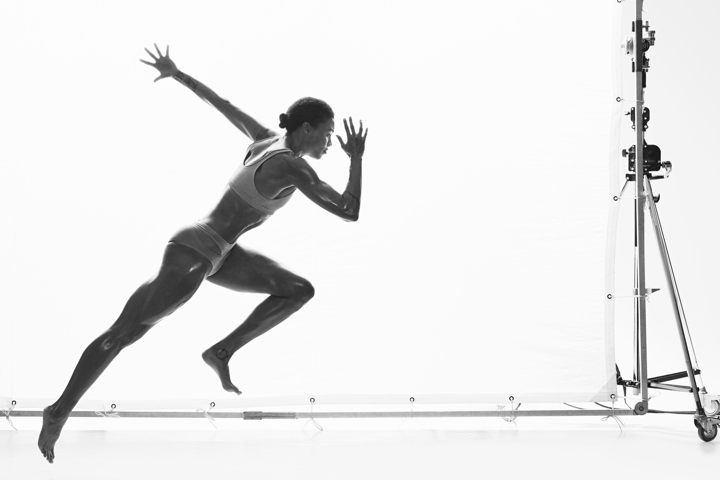 Athletic woman in running pose, captured in a dynamic black and white studio shot, showcasing power and physique with professional lighting.