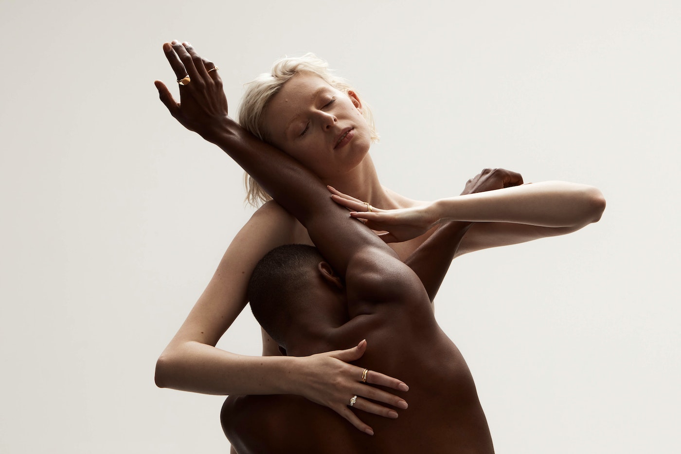 Interracial couple embracing in a photo studio with soft, neutral lighting and a minimalist aesthetic, showing intimacy and connection.