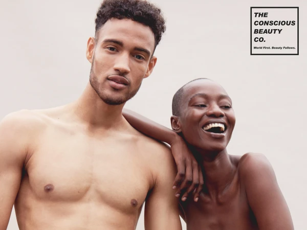 A shirtless man with short dark hair and a smiling woman with a shaved head posed against a plain light background.