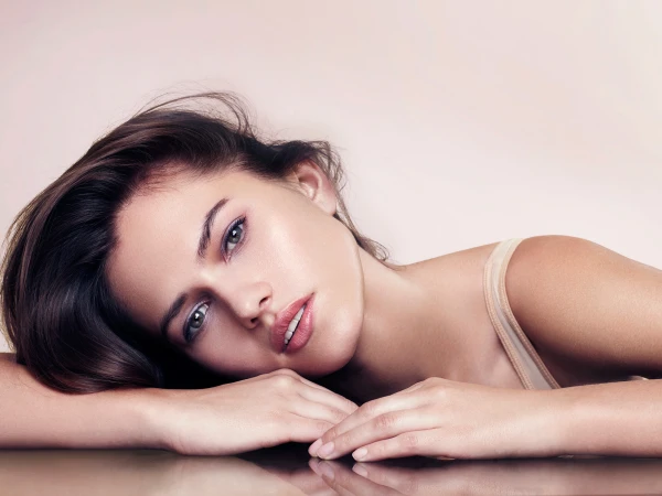 Close-up portrait of a woman resting her head on her crossed arms against a neutral background by Jen Wilding