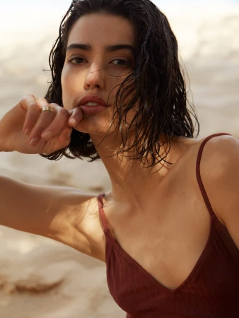 Close-up portrait of a woman with wet dark hair wearing a burgundy top against a sandy beach background by Jen Wilding
