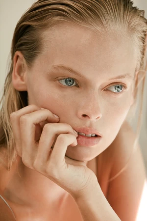 Close-up portrait of a woman with wet hair and blue eyes resting her hand on her chin, photographed by Jen Wilding.