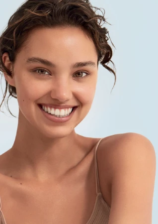 Close-up portrait of a smiling young woman with wet brown hair against a light blue backdrop.