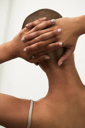 Close-up portrait of person with a shaved head holding hands behind their head showcasing colorful manicure