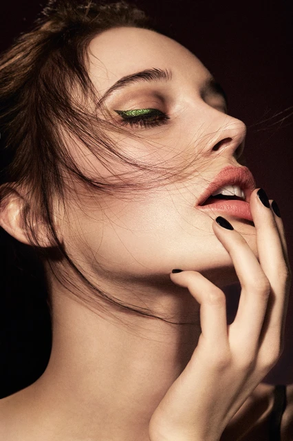 Close-up beauty shot of a fair-skinned woman with dramatic green eyeliner, slightly parted lips, and her hand near her face.