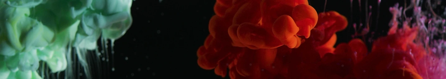 Vibrant plumes of red and green ink dispersing in water against a dark black background, captured by Vicki Lee.