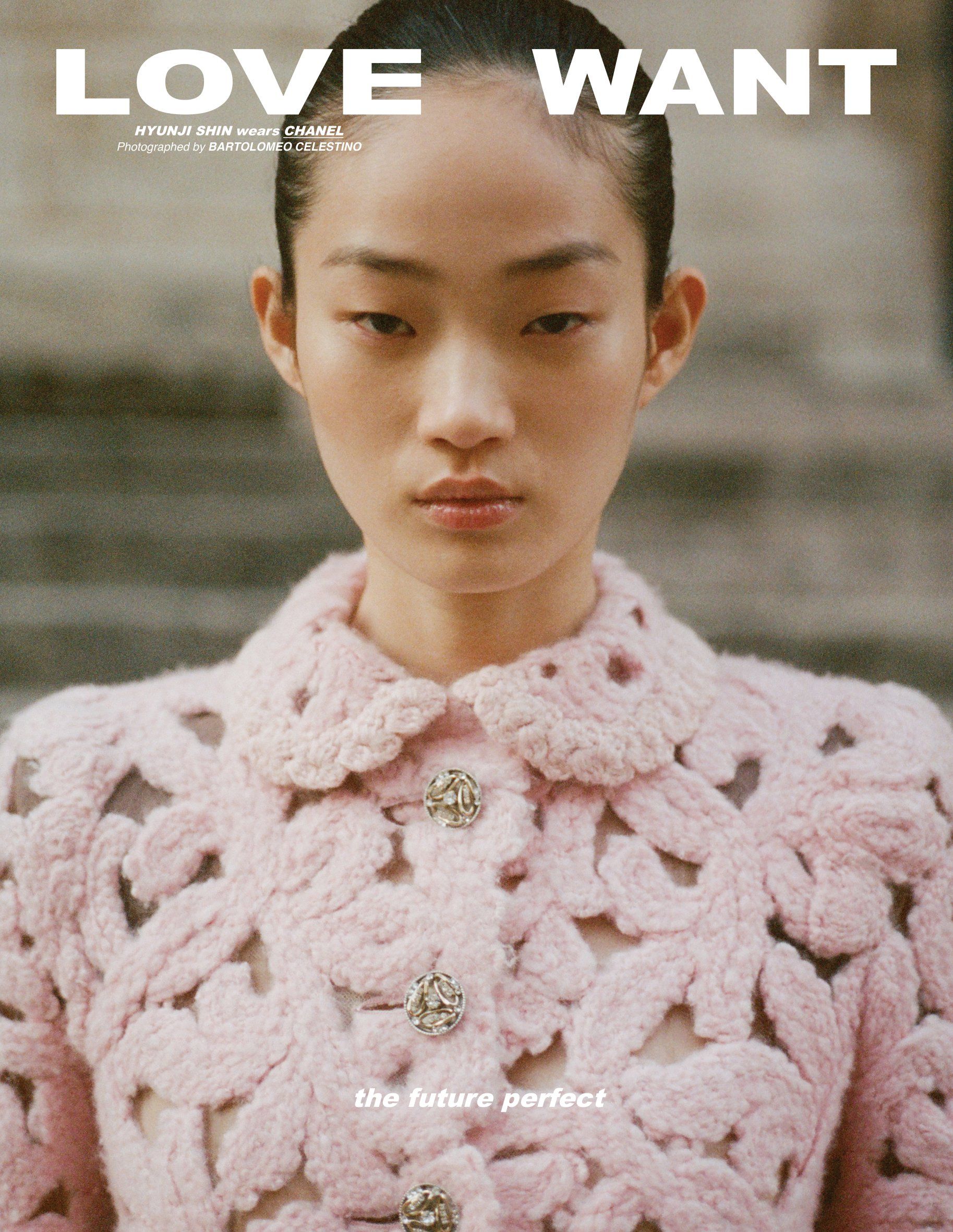 Close-up of an Asian woman with slicked-back hair wearing a pink crocheted jacket, staring intently into the camera in a fashion editorial.
