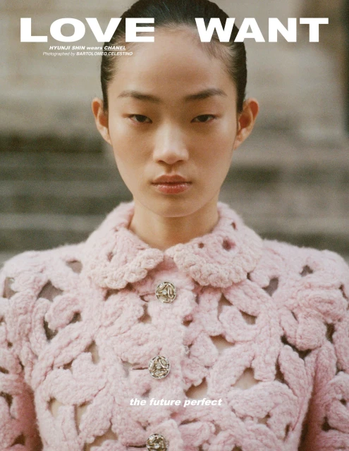 Close-up of an Asian woman with slicked-back hair wearing a pink crocheted jacket, staring intently into the camera in a fashion editorial.