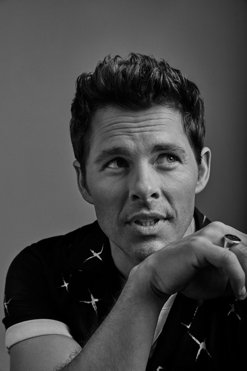 Monochrome portrait of a handsome adult male with dark hair, wearing a patterned short-sleeve shirt, looking up in a photo studio.
