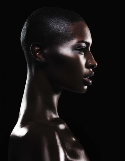 Profile portrait of African-American woman with shaved head and dark skin in beauty shot against a black background. Studio lighting.