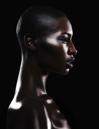 Profile portrait of a Black woman with a shaved head in dramatic low-key lighting against a dark background