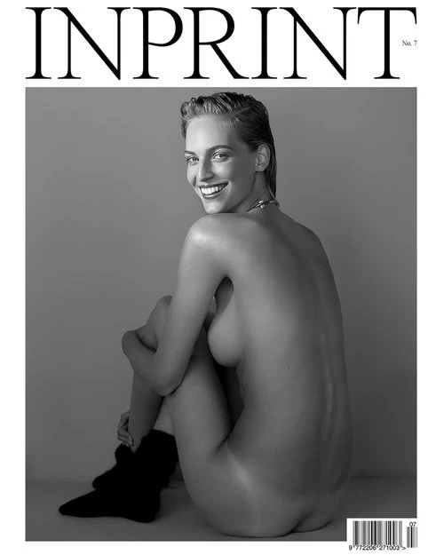 Black and white magazine cover featuring a smiling woman with short hair and black socks, sitting against a plain gray background.