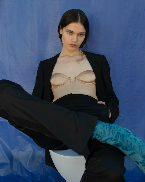 Model in black jacket and trousers with a nude bra top posing against a crinkled blue backdrop by photographer Holly Ward.