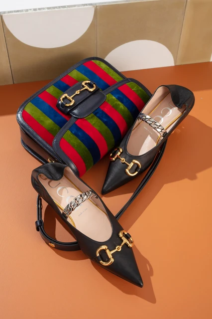 Fashion still life: A vertically striped handbag with gold hardware and two black leather point-toe flats with gold horse-bit details.