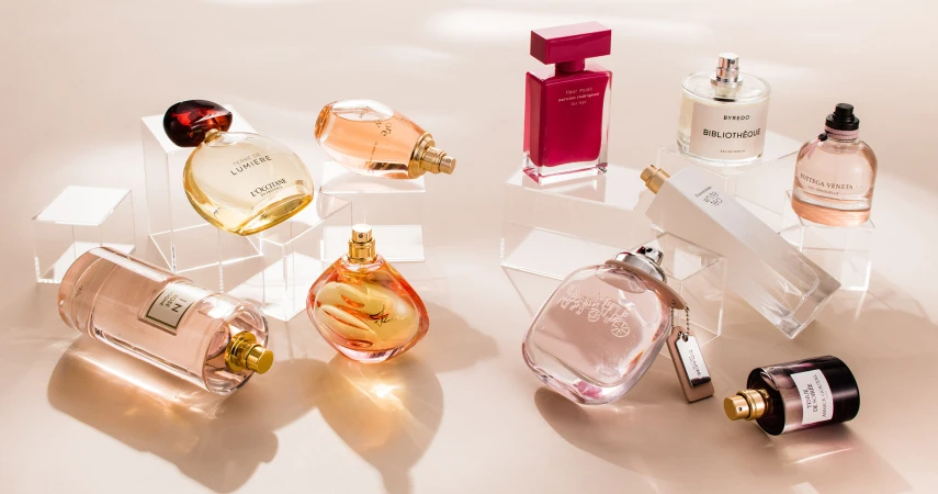 Arrangement of various perfume bottles on transparent acrylic stands, showcasing different shapes, colors, and brand names against a neutral backdrop.