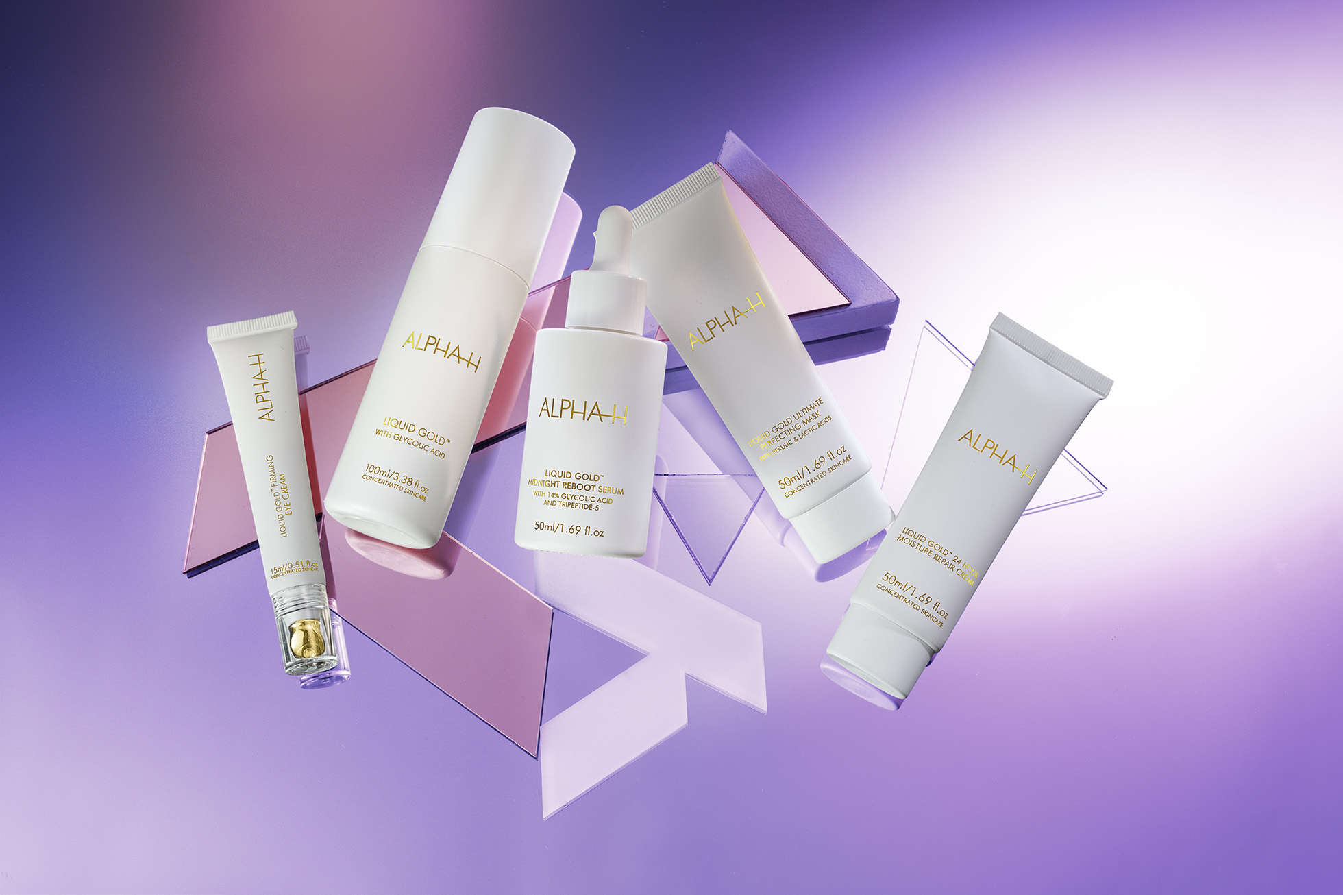 Several white and gold Alpha-H skincare product bottles and tubes are arranged on a reflective surface with a purple backdrop.