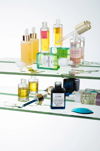 Beauty product bottles on glass shelves featuring serums and oils with various colors and textures in a brightly lit studio setting.