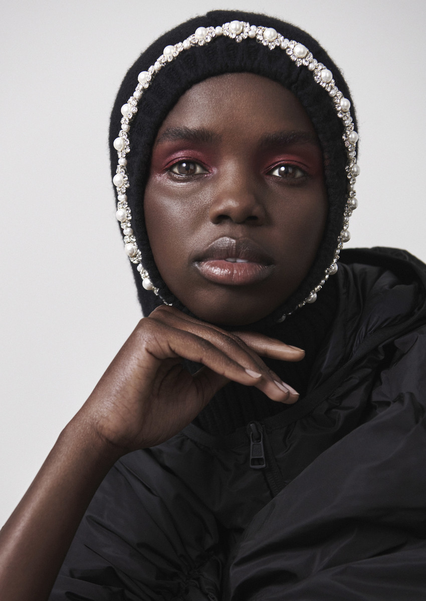 Close-up of an African woman in a black, pearl-trimmed knit balaclava and black jacket, set against a plain white backdrop.