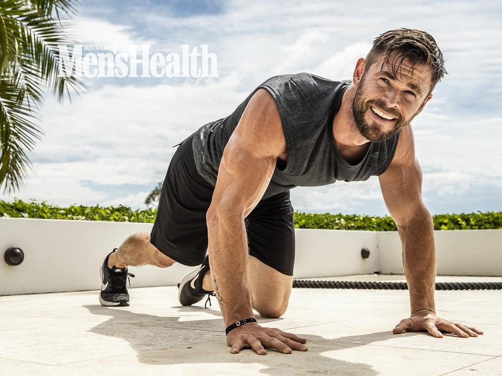 Muscular man, Chris Hemsworth, in workout attire does push-ups outside on a sunny day for an Australian Men's Health magazine cover.