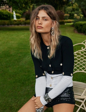Female model in black cropped cardigan and sequin shorts seated outdoors in a park by photographer Steven Chee