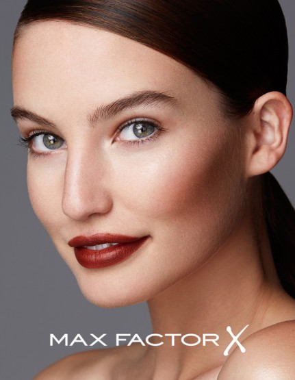 Close-up studio shot of a fair-skinned adult woman with dark red lipstick, glossy hair, and neutral expression, against a solid grey backdrop.