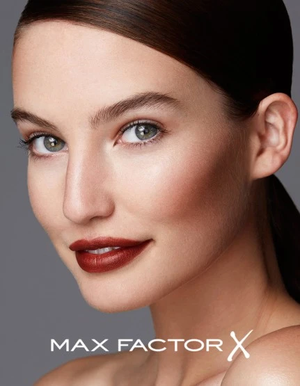 Close-up studio shot of a fair-skinned adult woman with dark red lipstick, glossy hair, and neutral expression, against a solid grey backdrop.
