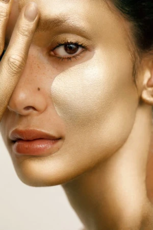 Close-up portrait of a woman with metallic gold paint on her face and hand by photographer Tane Coffin