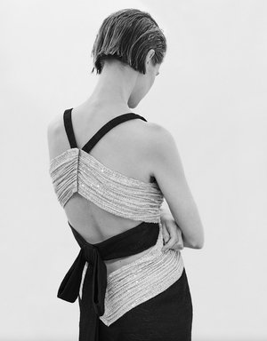 Model with short wet-look hair wearing a black and silver sequined gown with a bow back detail