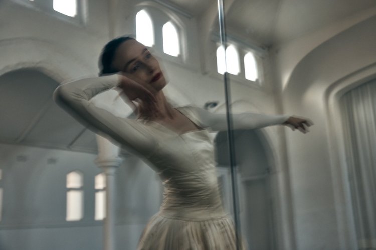 A woman in a white dress strikes a pose in a bright room with large arched windows, captured with motion blur and a shallow depth of field.
