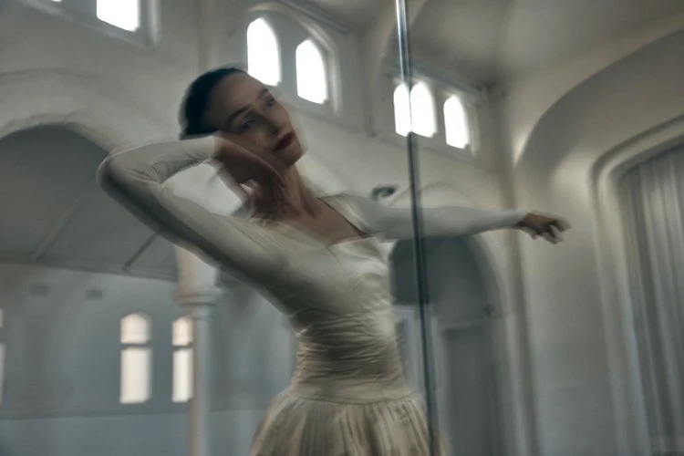 A woman in a white dress strikes a pose in a bright room with large arched windows, captured with motion blur and a shallow depth of field.