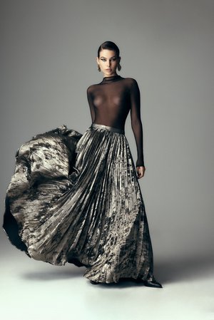 Model in a black sheer top and pleated metallic skirt against a grey background styled by Karla Clarke