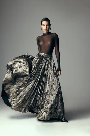 Model in a black sheer top and pleated metallic skirt against a grey background styled by Karla Clarke