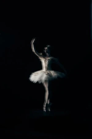 Woman in white ballet tutu poses gracefully en pointe in a dimly lit dance studio, creating a sense of artistic movement and elegance.