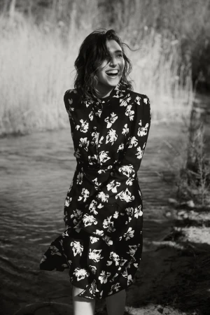 Smiling woman in a patterned floral dress standing near a riverbank
