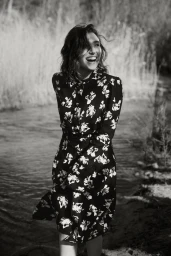 Smiling woman in a patterned floral dress standing near a riverbank