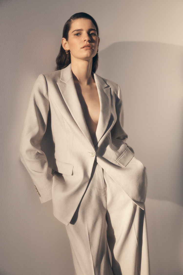Woman in oversized neutral pantsuit poses against a gradient background in a studio fashion shot for Visie creative platform.