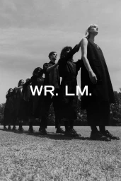 Monochrome image of a line of people standing in a row outdoors on grass, wearing dark apparel, directed by Toby Rupert