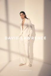 Model wearing a white pantsuit standing in a bright corner with window shadow patterns by Toby Rupert