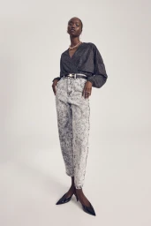 Black woman wearing a dark wrap top, acid wash jeans, and black slingback heels against a light grey seamless backdrop.