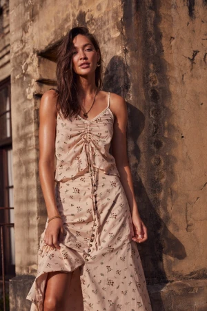Woman wearing a floral camisole top and matching midi skirt standing outdoors against a weathered stone wall in Sydney