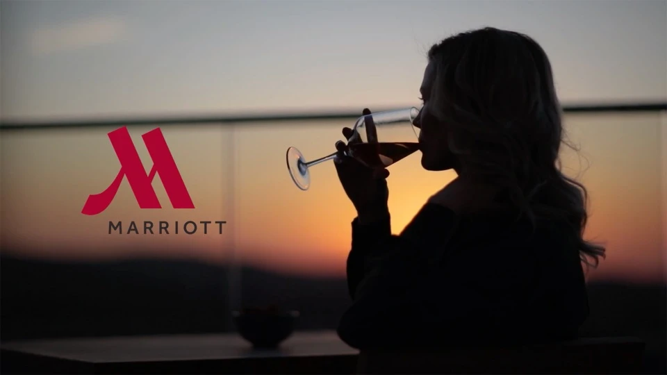 Silhouette of a woman drinking wine with a Marriott logo in the background, set against an outdoor sunset backdrop.