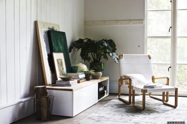 Interior shot featuring a white modern armchair with footstool, low sideboard with books and art, and large windows by Paul Barbera.