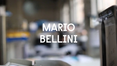 Bold white typography displaying MARIO BELLINI centered over an indistinct, softly blurred workshop or office interior background.