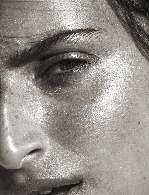 Close-up portrait of an adult female's face in black and white, showcasing skin texture, eye detail, and natural light, highlighting beauty.