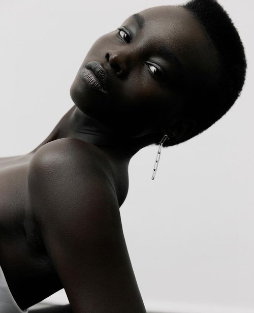 Close-up studio shot of a beautiful Black woman with short hair, wearing a silver earring, against a plain white background. Minimalist aesthetic.