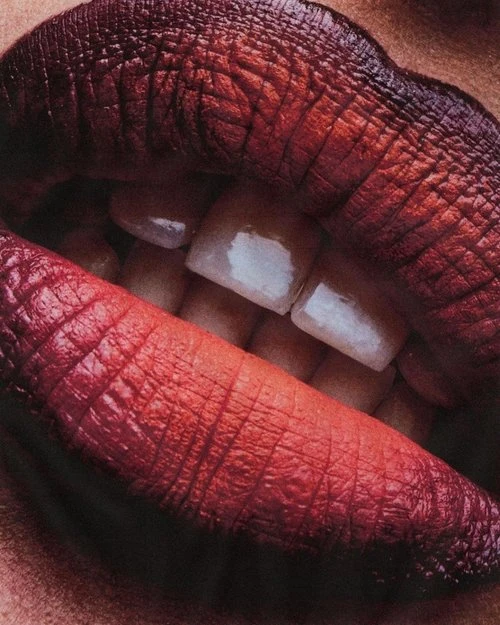 Close-up studio shot of a woman's lips, showcasing vibrant red lipstick with a dark ombré effect, highlighting the teeth and mouth.