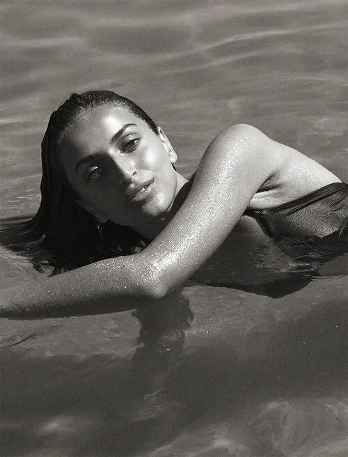 Monochrome portrait of a woman submerged in water, her wet arm resting across the surface with droplets visible.