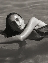 Monochrome portrait of a woman submerged in water, her wet arm resting across the surface with droplets visible.