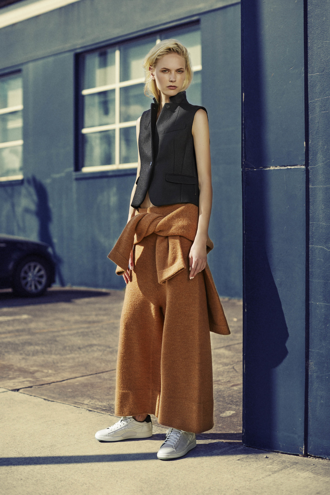 Model standing outdoors wearing a black vest and brown wide leg pants styled by Kate Gaskin in Sydney.