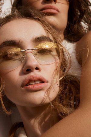 Close-up shot of two women in sunglasses with a light, warm color grade. One woman is slightly behind the other.